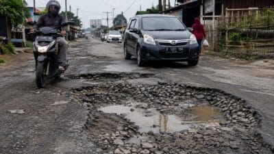 Pengendara melintasi jalan rusak yang berpotensi membahayakan keselamatan pengguna jalan.
